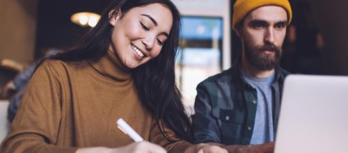 Što čini kvalitetan copy koji će privući publiku i ostvariti prodaju - nasmejana devojka i mladić sa žutom kapom i laptopom u kafiću pripremaju blog